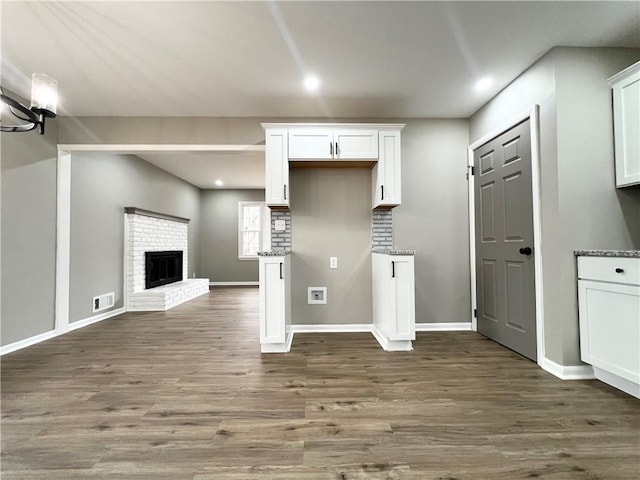 kitchen with visible vents, dark wood-style floors, light stone countertops, a brick fireplace, and white cabinetry