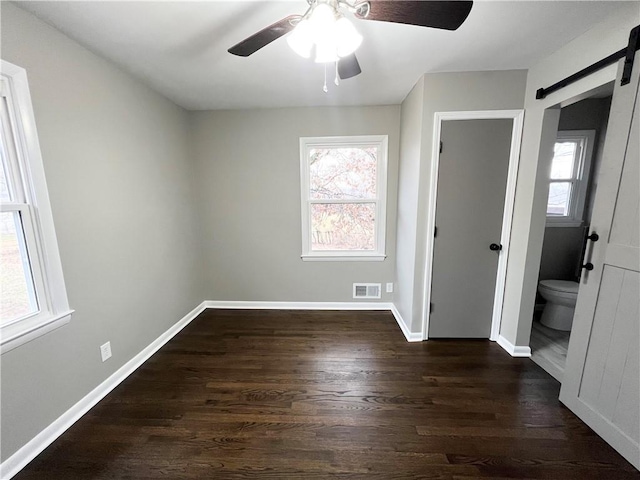 unfurnished bedroom featuring dark wood-style floors, a barn door, multiple windows, and visible vents