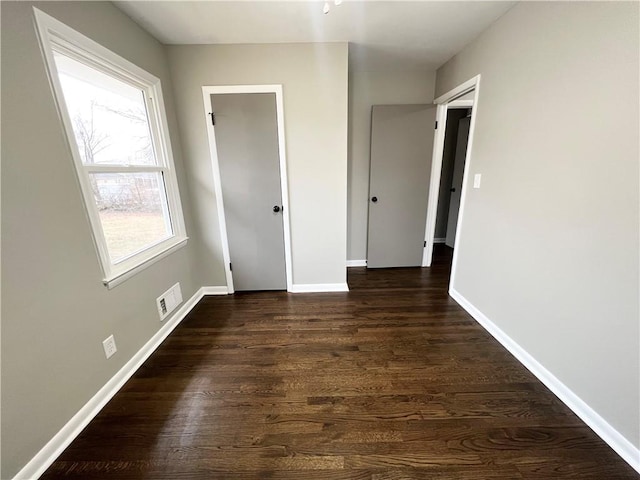 unfurnished room featuring dark wood-style flooring, visible vents, and baseboards