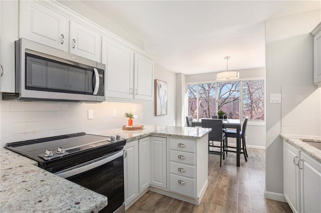 kitchen with stainless steel appliances, tasteful backsplash, white cabinetry, wood finished floors, and a peninsula