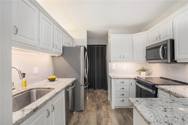 kitchen with light wood finished floors, decorative backsplash, stainless steel appliances, white cabinetry, and a sink