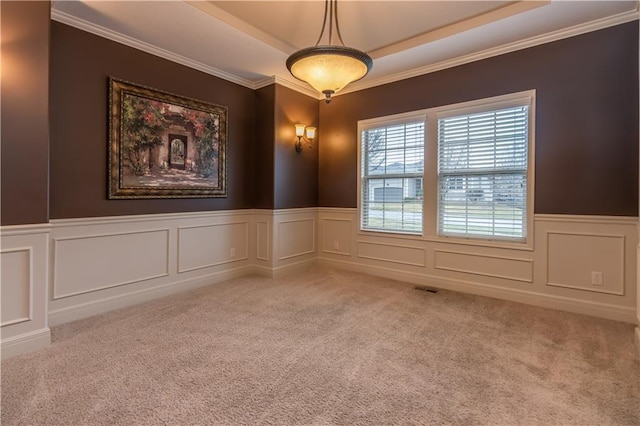 unfurnished room with visible vents, a tray ceiling, wainscoting, crown molding, and light carpet