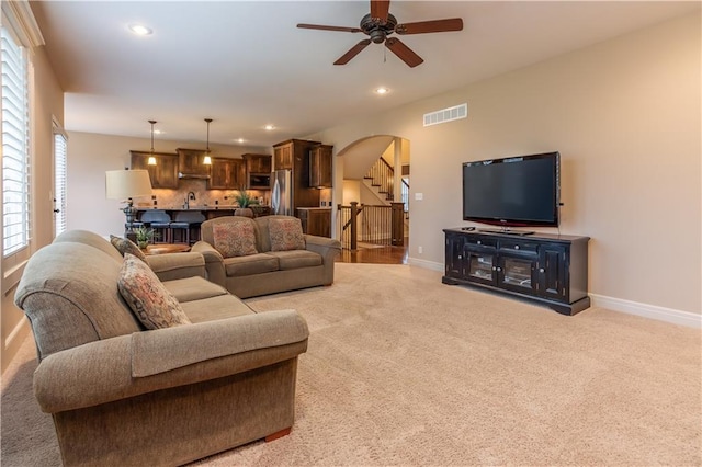 living area featuring visible vents, baseboards, stairs, light carpet, and arched walkways