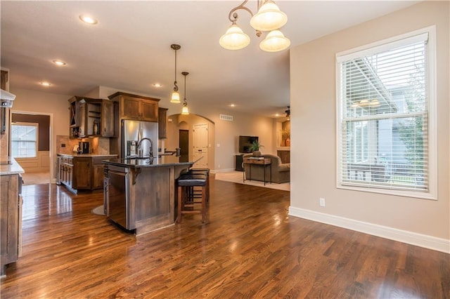 kitchen featuring a kitchen bar, stainless steel refrigerator with ice dispenser, open floor plan, dark wood-style floors, and arched walkways