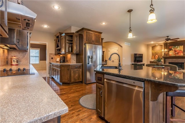 kitchen with a sink, open shelves, arched walkways, stainless steel appliances, and dark wood-style flooring