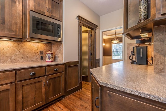 kitchen with dark wood-type flooring, stainless steel microwave, backsplash, wainscoting, and dark brown cabinets