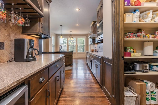 kitchen featuring dark wood-style floors, a sink, dark brown cabinets, decorative light fixtures, and backsplash