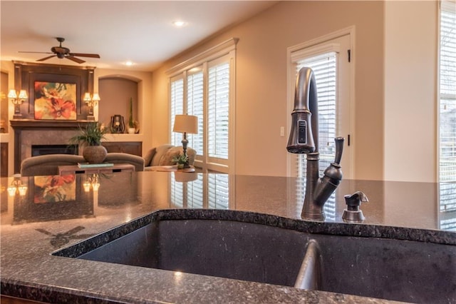 kitchen with dark stone countertops, a fireplace, a ceiling fan, and a sink