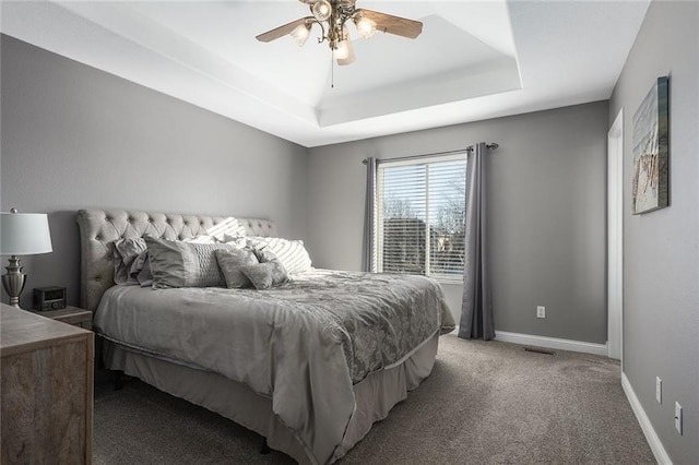 carpeted bedroom featuring baseboards, a raised ceiling, visible vents, and a ceiling fan