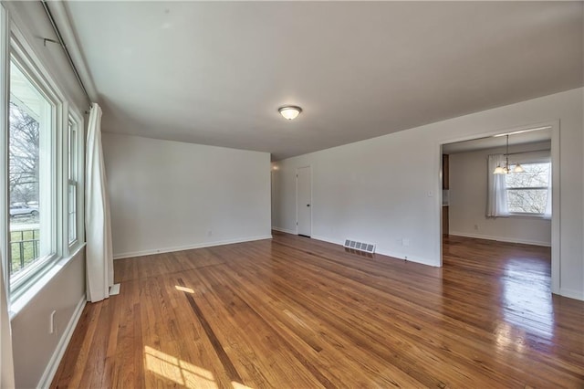 empty room with baseboards, a notable chandelier, visible vents, and wood finished floors