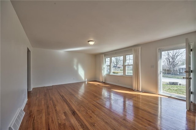 unfurnished room featuring wood-type flooring, visible vents, and baseboards