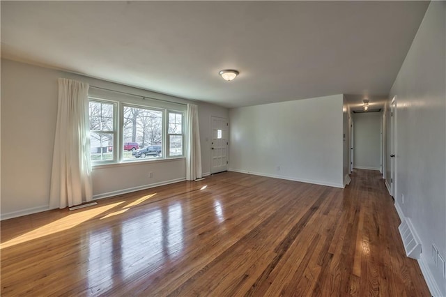 spare room with dark wood-type flooring, visible vents, and baseboards