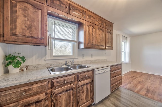 kitchen featuring light countertops, white dishwasher, a sink, and light wood-style flooring