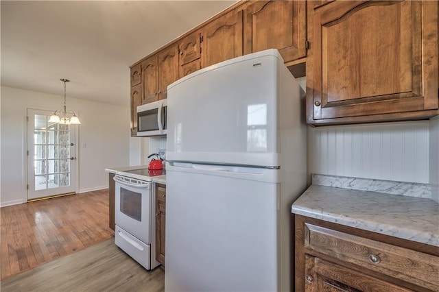 kitchen featuring white appliances, brown cabinetry, hanging light fixtures, light wood-type flooring, and a chandelier