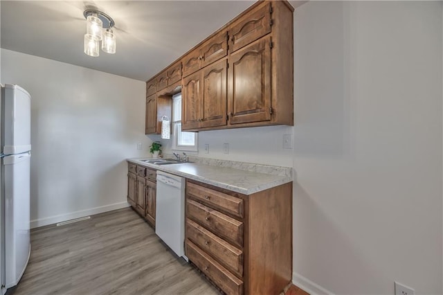 kitchen featuring white appliances, a sink, baseboards, light countertops, and light wood finished floors