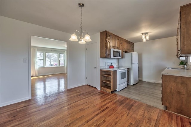 kitchen with white appliances, wood finished floors, light countertops, a chandelier, and a sink