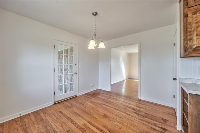 unfurnished dining area featuring an inviting chandelier, light wood-style flooring, and baseboards