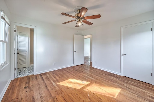 unfurnished bedroom featuring baseboards, multiple windows, a ceiling fan, and light wood-style floors