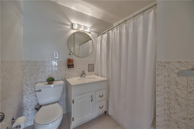 bathroom with tile walls, a wainscoted wall, vanity, and toilet