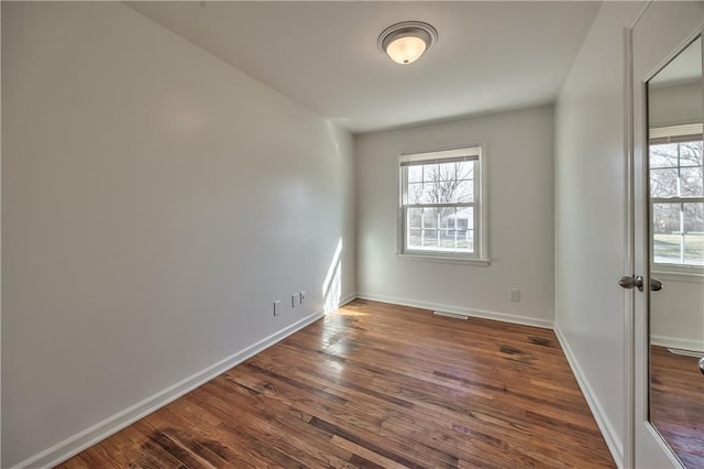 empty room with a healthy amount of sunlight, visible vents, baseboards, and dark wood finished floors