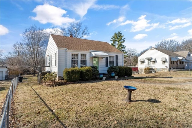 view of front facade featuring a chimney, a shingled roof, a front yard, and fence