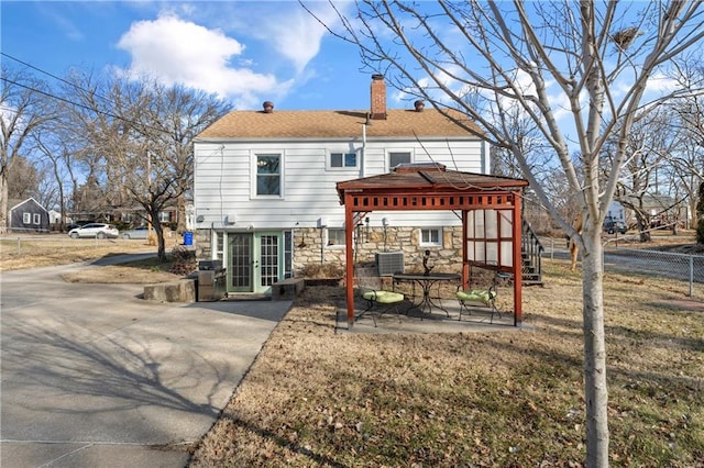 back of house featuring stone siding, a patio, fence, a gazebo, and a chimney