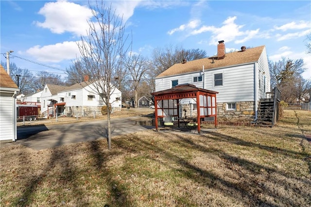 rear view of property featuring a gazebo, stairway, a lawn, and a chimney