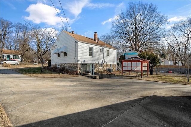 view of home's exterior featuring stone siding, an outbuilding, a chimney, and fence