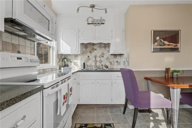 kitchen featuring dark countertops, white appliances, white cabinetry, and a sink