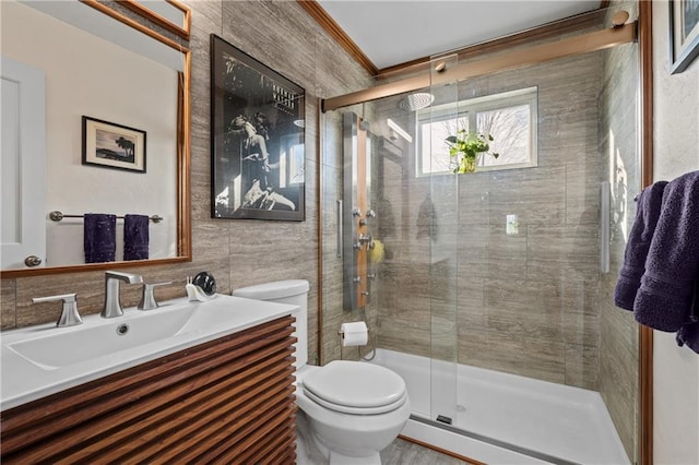 bathroom with vanity, a stall shower, ornamental molding, tile walls, and toilet