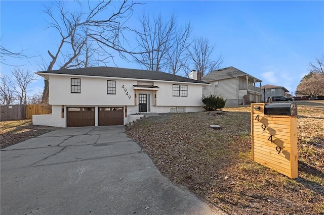 raised ranch with an attached garage, concrete driveway, and fence