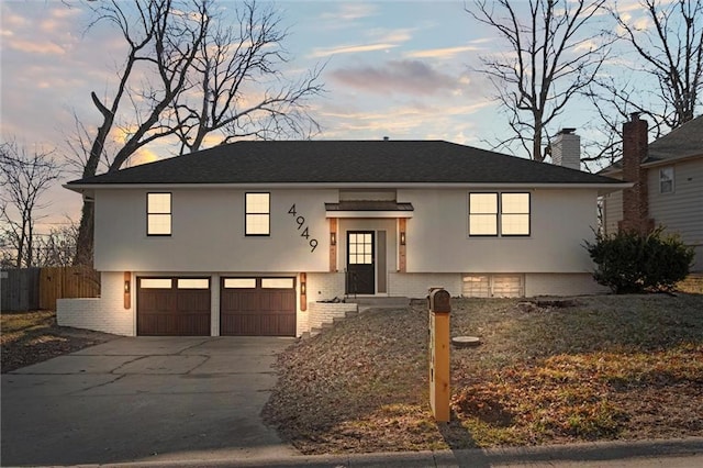 split foyer home featuring brick siding, fence, stucco siding, a garage, and driveway