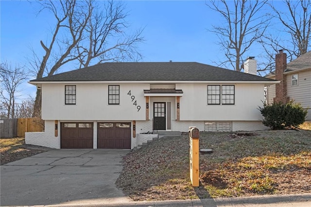 split foyer home featuring fence, driveway, a chimney, a garage, and brick siding