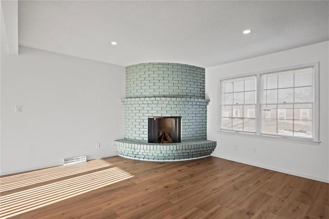 unfurnished living room featuring visible vents, a brick fireplace, baseboards, wood finished floors, and a textured ceiling