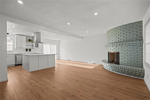 unfurnished living room with plenty of natural light, a textured ceiling, a fireplace, and light wood finished floors