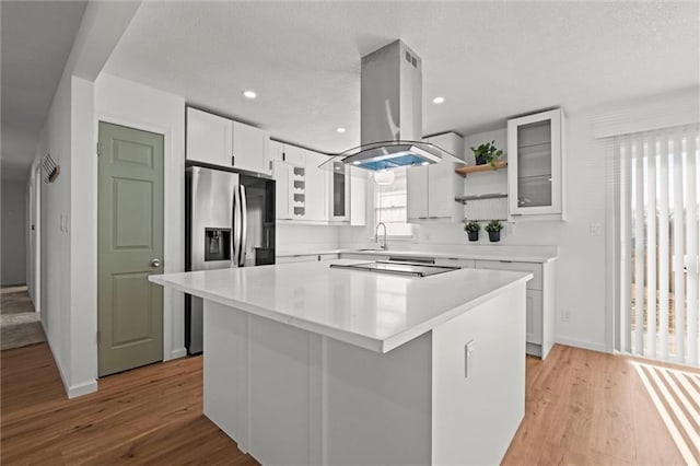 kitchen with light wood-type flooring, island exhaust hood, a sink, a center island, and white cabinetry