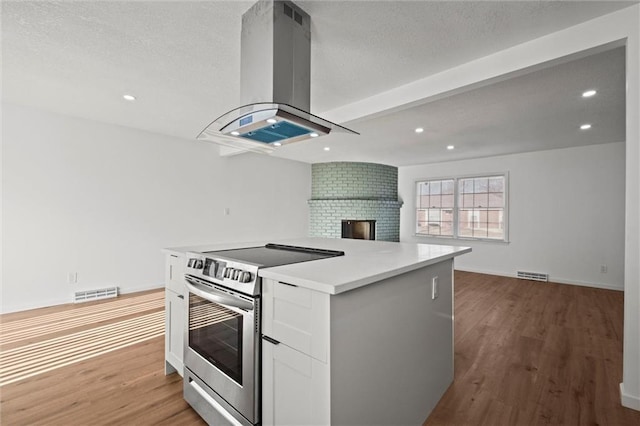 kitchen with island exhaust hood, visible vents, a kitchen island, and stainless steel electric range