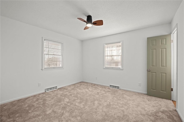 carpeted empty room featuring visible vents, baseboards, a textured ceiling, and ceiling fan