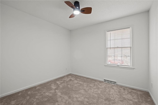 empty room with visible vents, a textured ceiling, carpet floors, baseboards, and ceiling fan