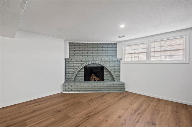 unfurnished living room featuring a fireplace, a textured ceiling, baseboards, and wood finished floors