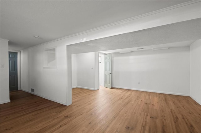 below grade area with visible vents, baseboards, wood finished floors, and crown molding