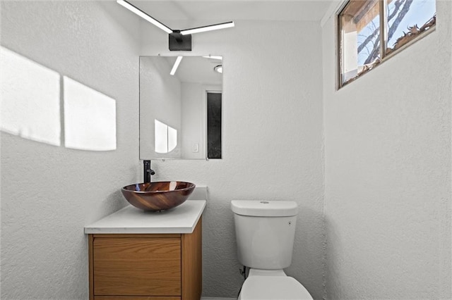 bathroom with toilet, vanity, and a textured wall