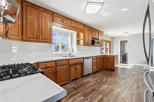 kitchen with brown cabinets, a sink, dark wood-style floors, appliances with stainless steel finishes, and light countertops