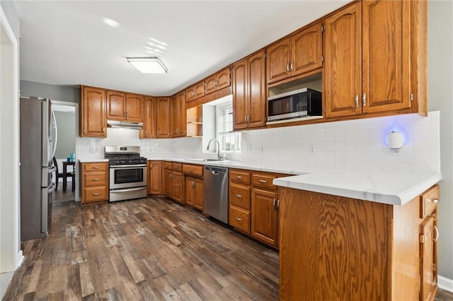 kitchen featuring under cabinet range hood, stainless steel appliances, brown cabinets, and a sink