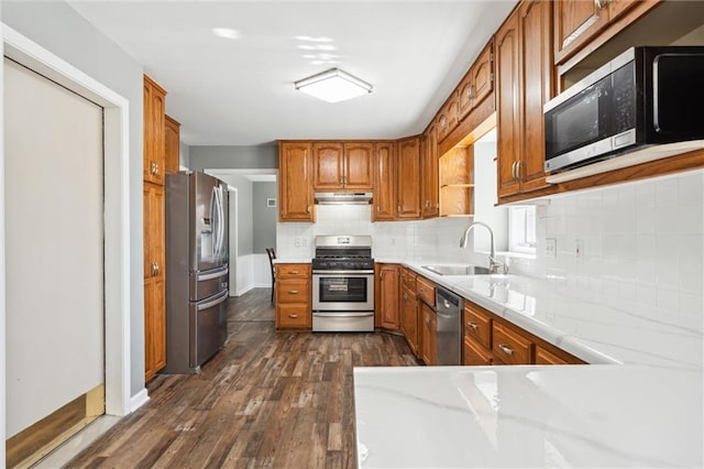 kitchen featuring dark wood-type flooring, under cabinet range hood, light countertops, appliances with stainless steel finishes, and a sink