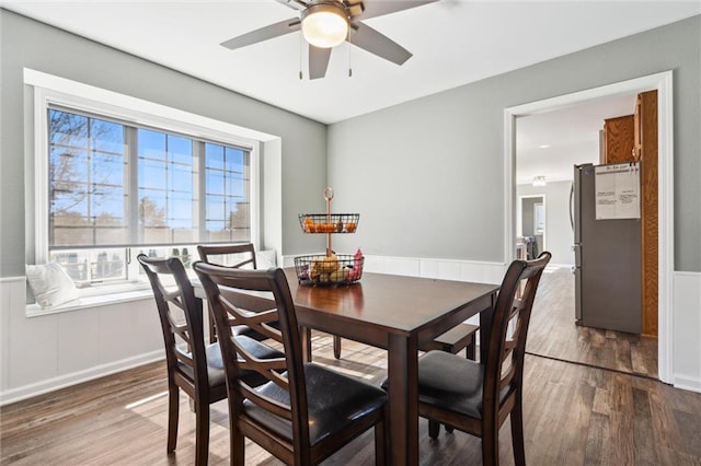 dining room featuring a ceiling fan, wood finished floors, and a wainscoted wall