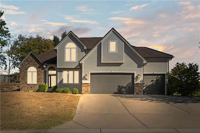 view of front of home featuring stone siding, a yard, concrete driveway, and stucco siding