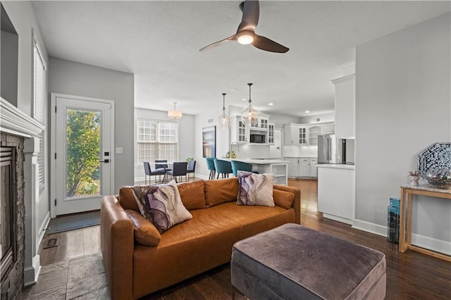 living room featuring a fireplace, visible vents, a ceiling fan, wood finished floors, and baseboards