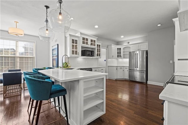 kitchen featuring dark wood finished floors, a sink, black microwave, a peninsula, and high end refrigerator