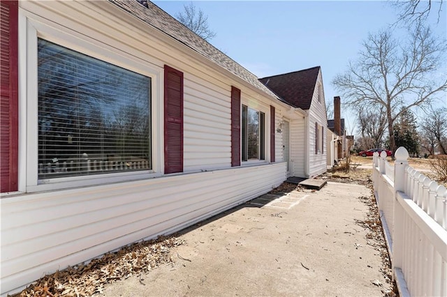 view of side of home with a patio, a shingled roof, and fence